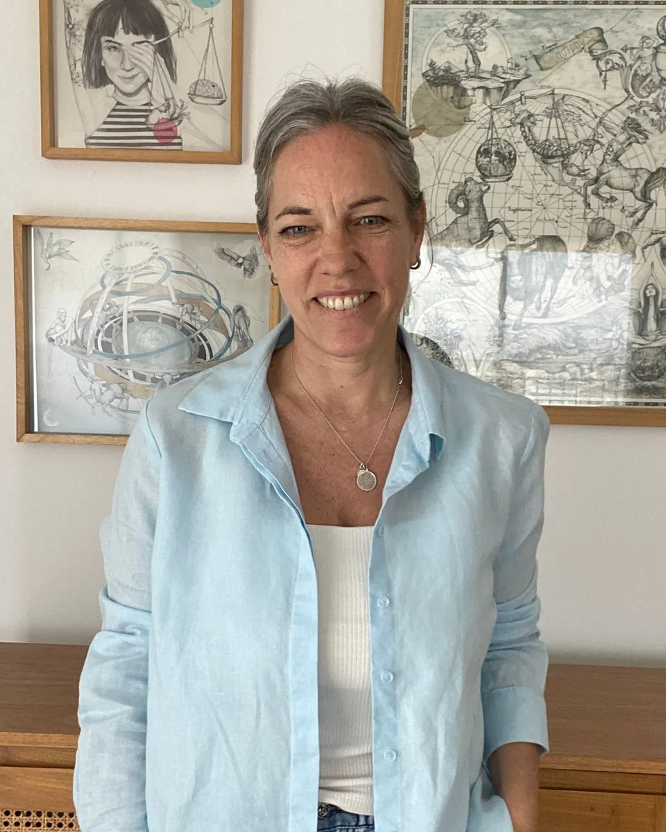 Erica, sonriente, con camisa celeste, delante de dibujos enmarcados